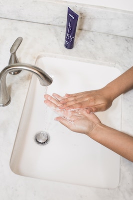 zwei Hände beim Händewaschen über einem weißen Waschbecken mit moderner Edelstahl Wasserarmatur